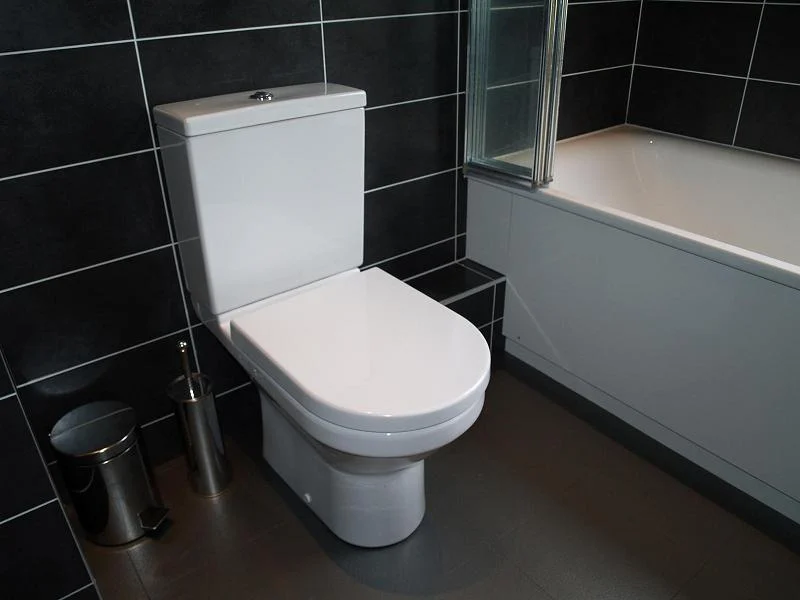 White close-coupled toilet in black-tiled bathroom — toilet installation Ealing