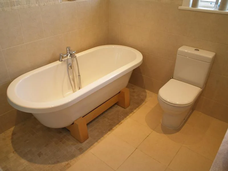 Ealing bathroom installation showing freestanding bath and close-coupled toilet with cream stone-effect tiles